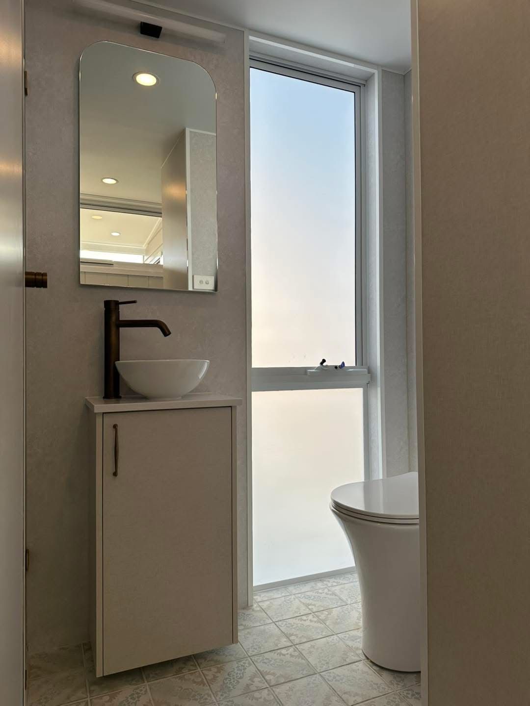 Modern bathroom with a white sink, black faucet, arched mirror, and frosted window.