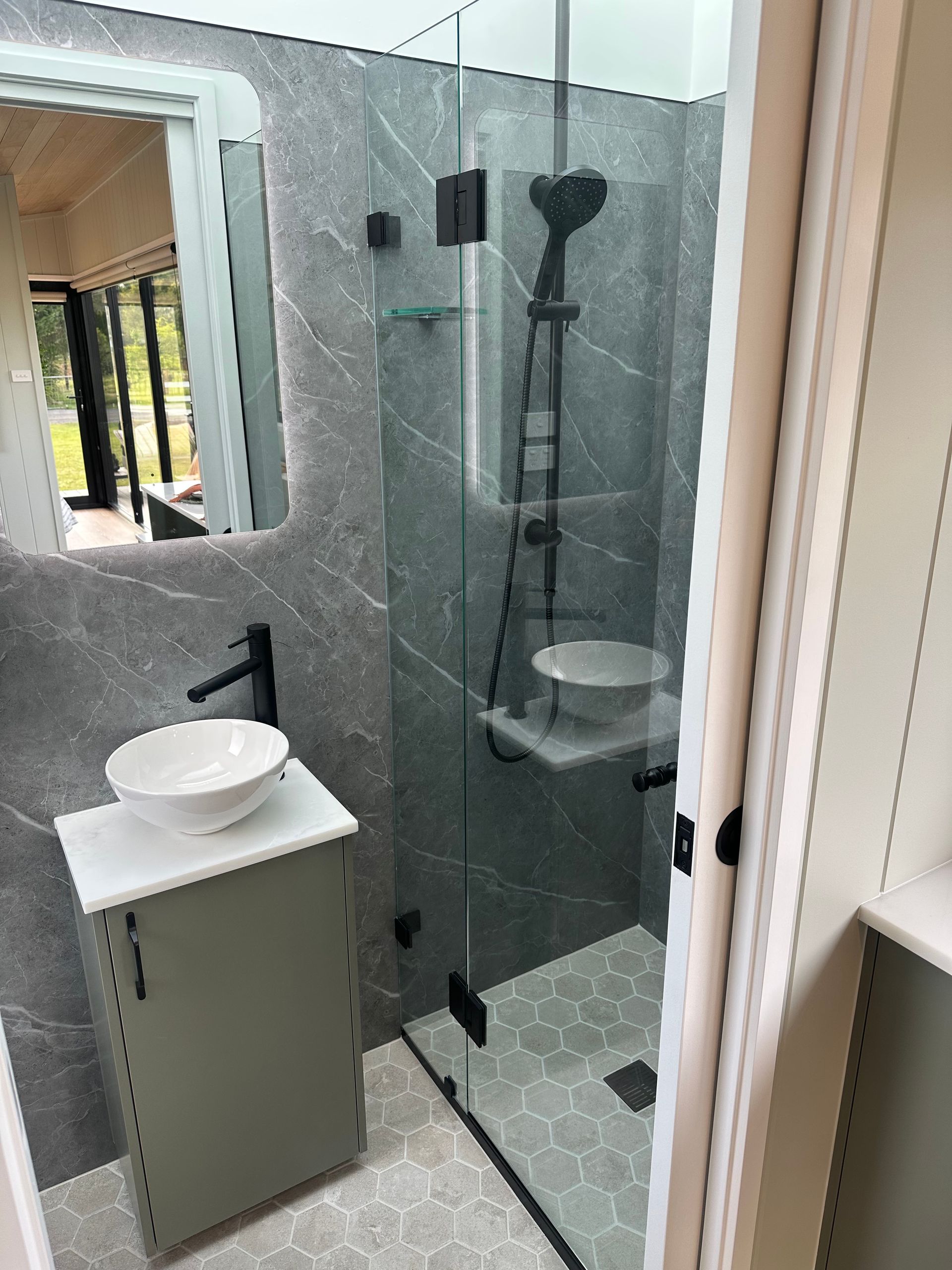 Bathroom with gray tile, shower, sink, black fixtures, and a small, green cabinet.