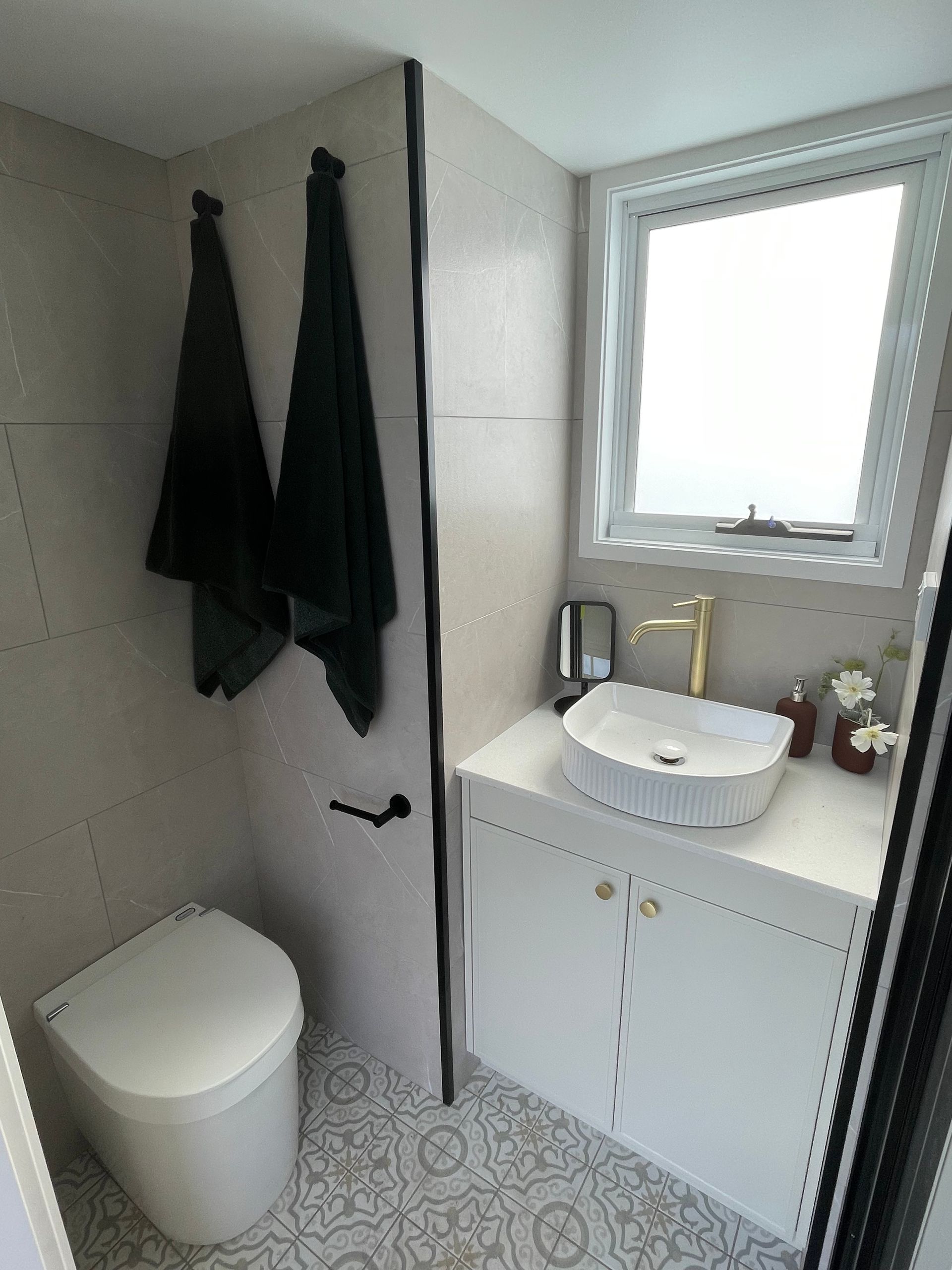 Small bathroom with a white toilet, sink, and vanity, with patterned flooring. Two dark towels are hanging on the wall.