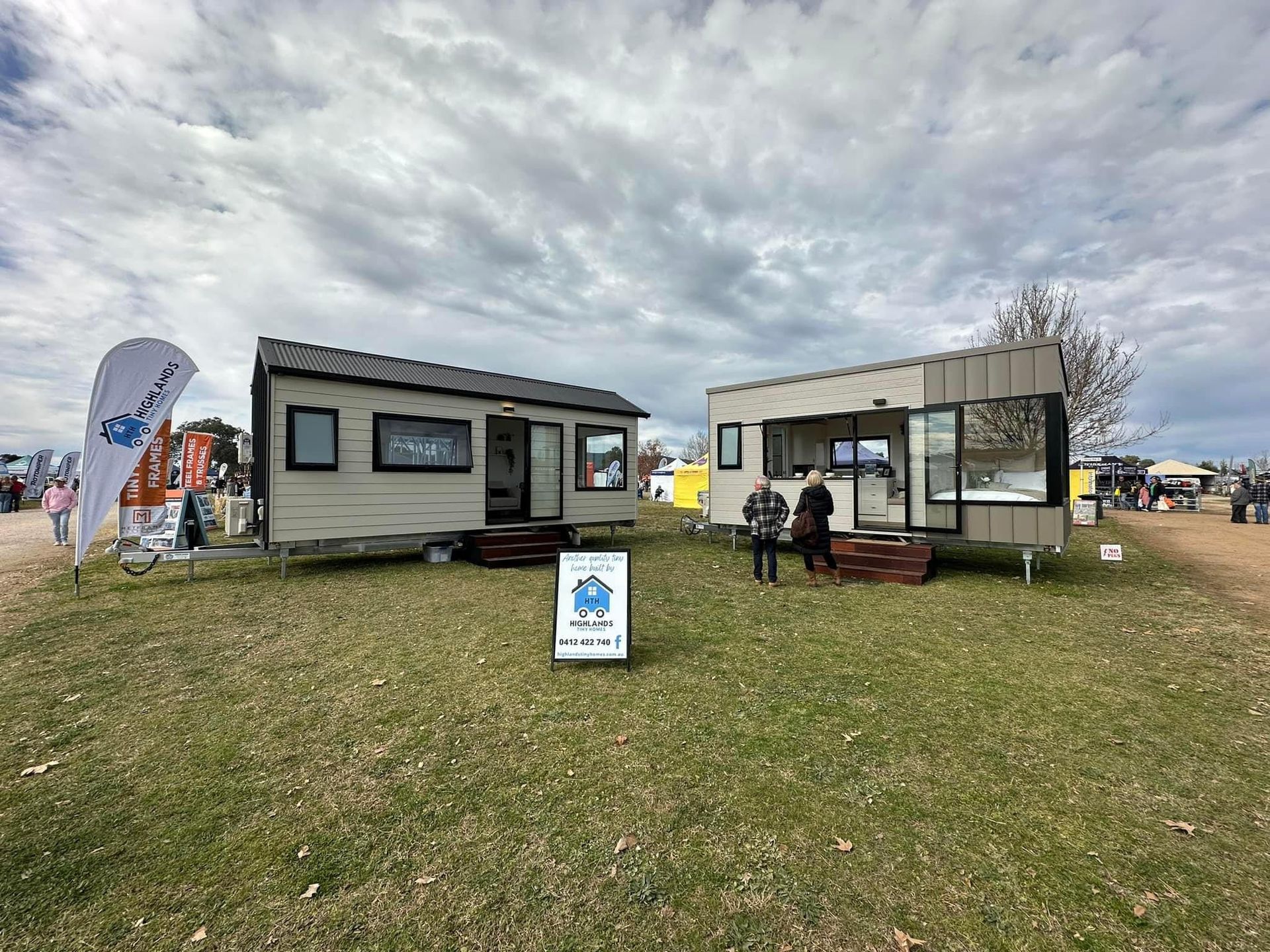 Two tiny houses on display at an outdoor event, with visitors present.