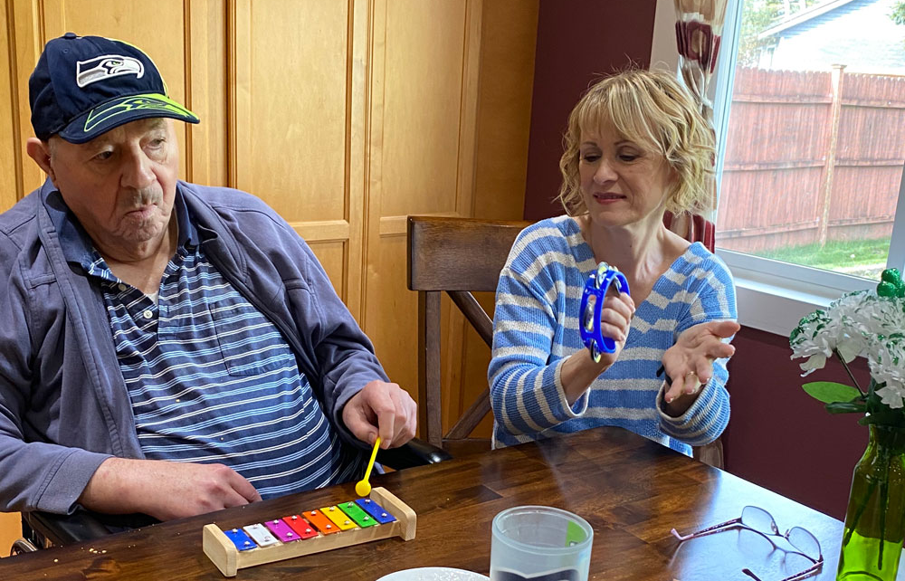A man is sitting at a table holding a bottle of wine and a woman is holding a balloon.