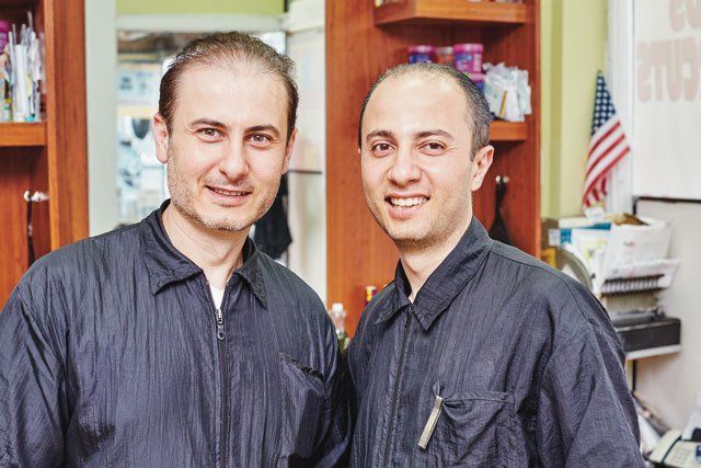 Two men are posing for a picture in a barber shop.