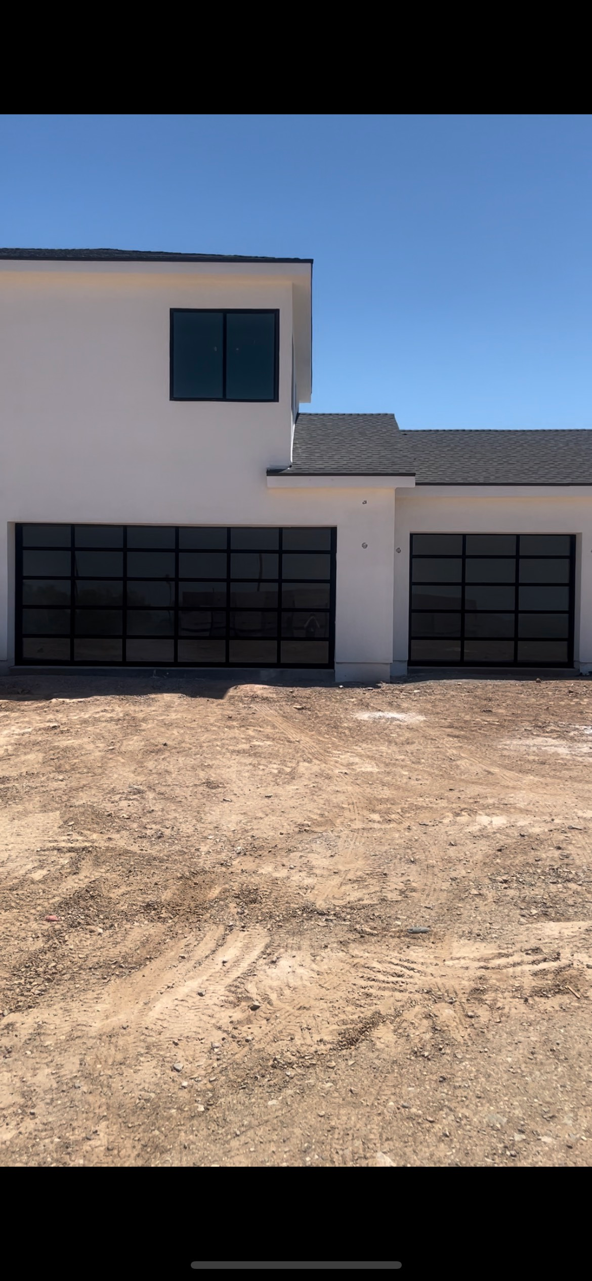 A white house with black garage doors is sitting on top of a dirt field.