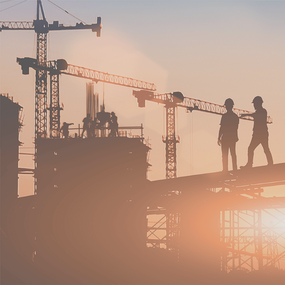 Construction site at sunset with workers on scaffolding and cranes.
