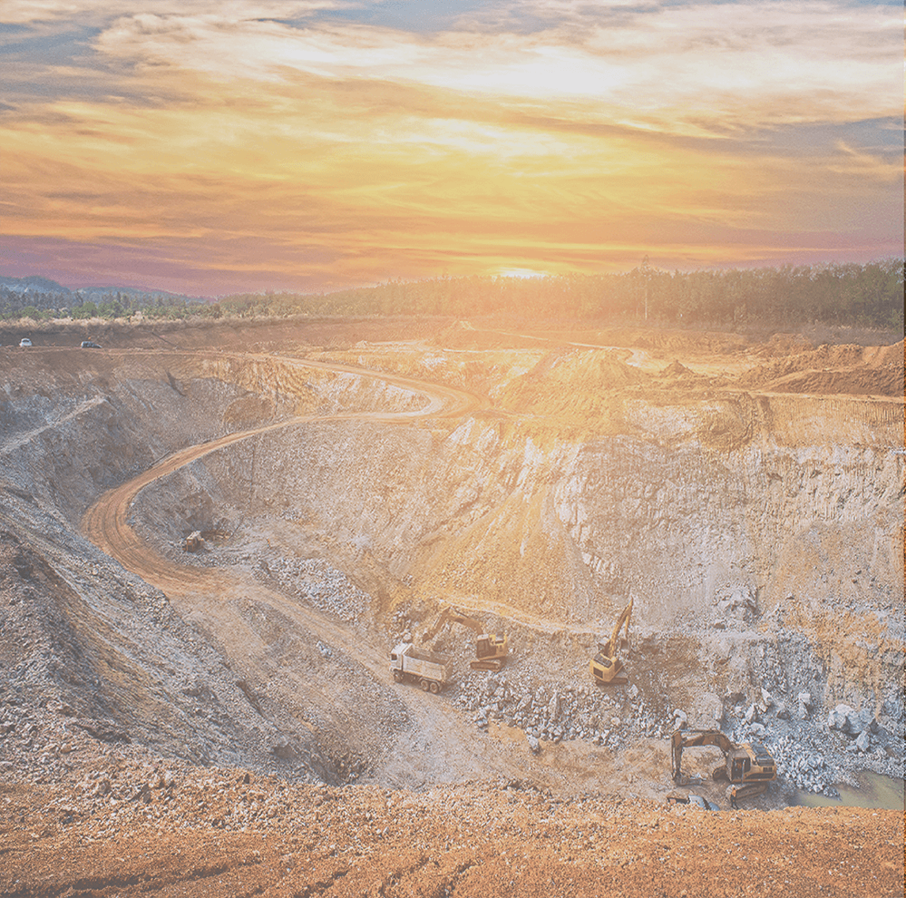 Open-pit mine at sunset with heavy machinery operating in the large excavation.
