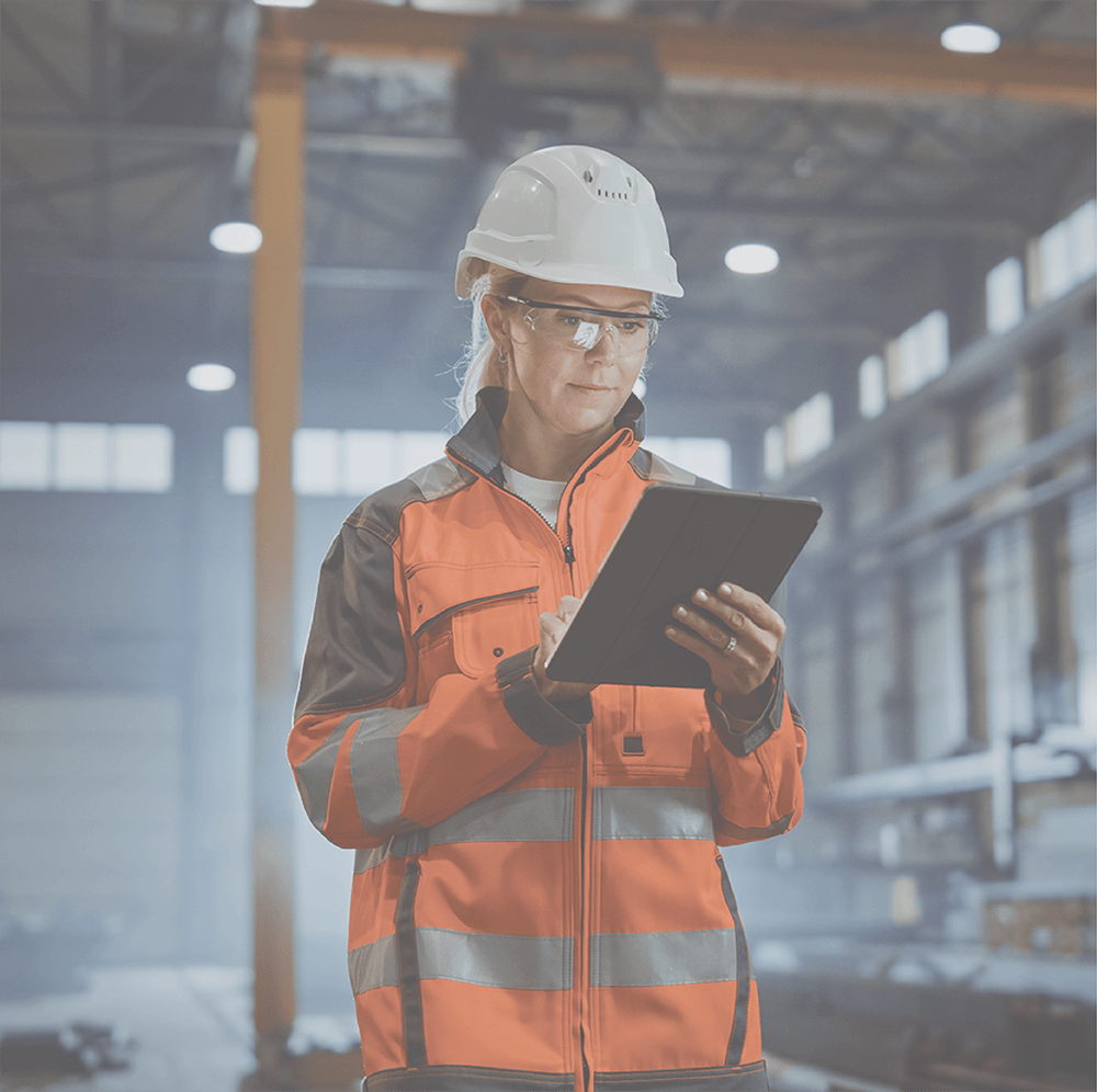 Woman in safety gear uses a tablet in a factory.