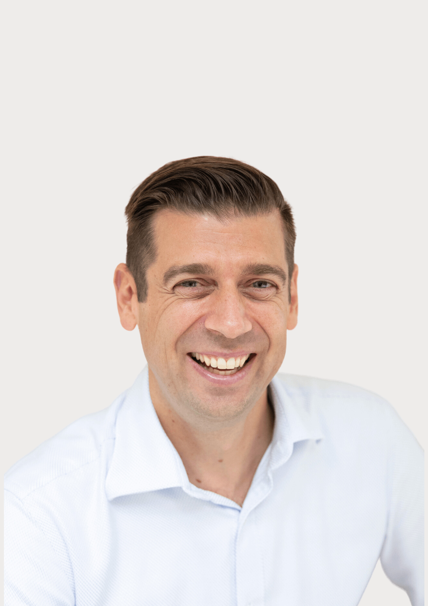 Man with dark hair and a light blue shirt smiles at the camera.