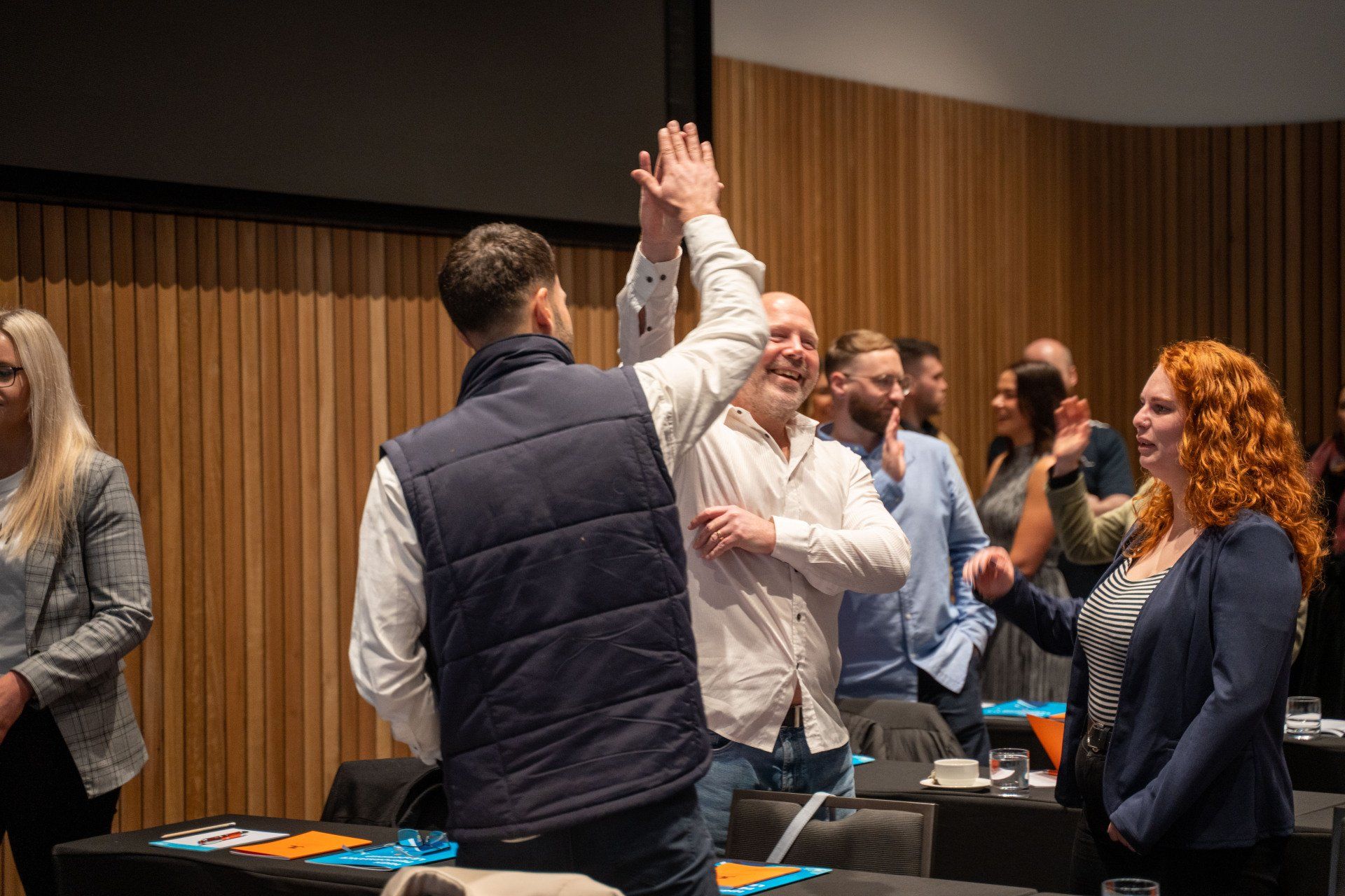Group of people high-fiving in a wood-paneled room, celebrating.