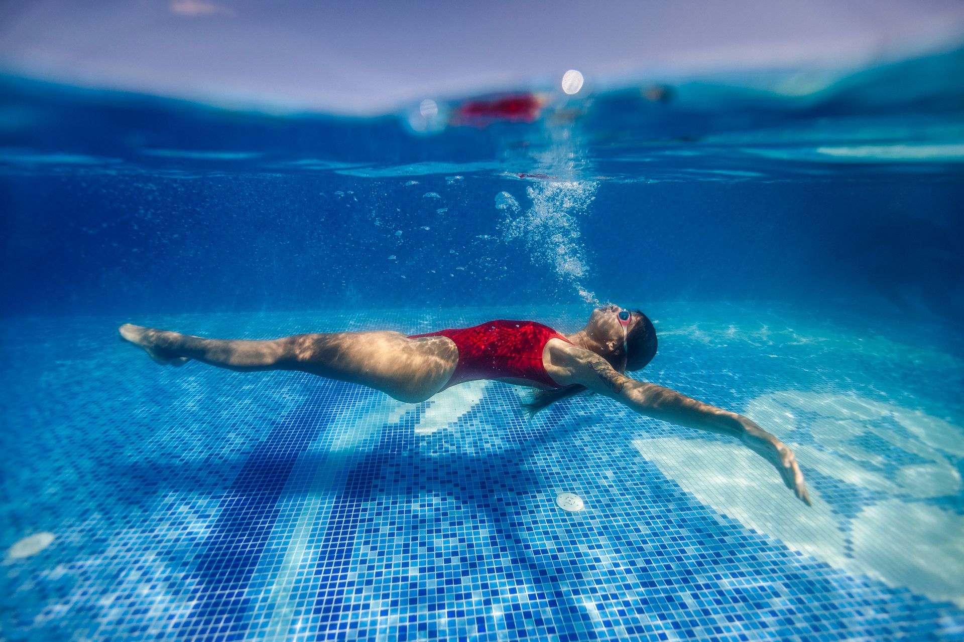 Man in a swimming cap supports a woman in a red swimsuit in a pool; they are smiling and laughing.