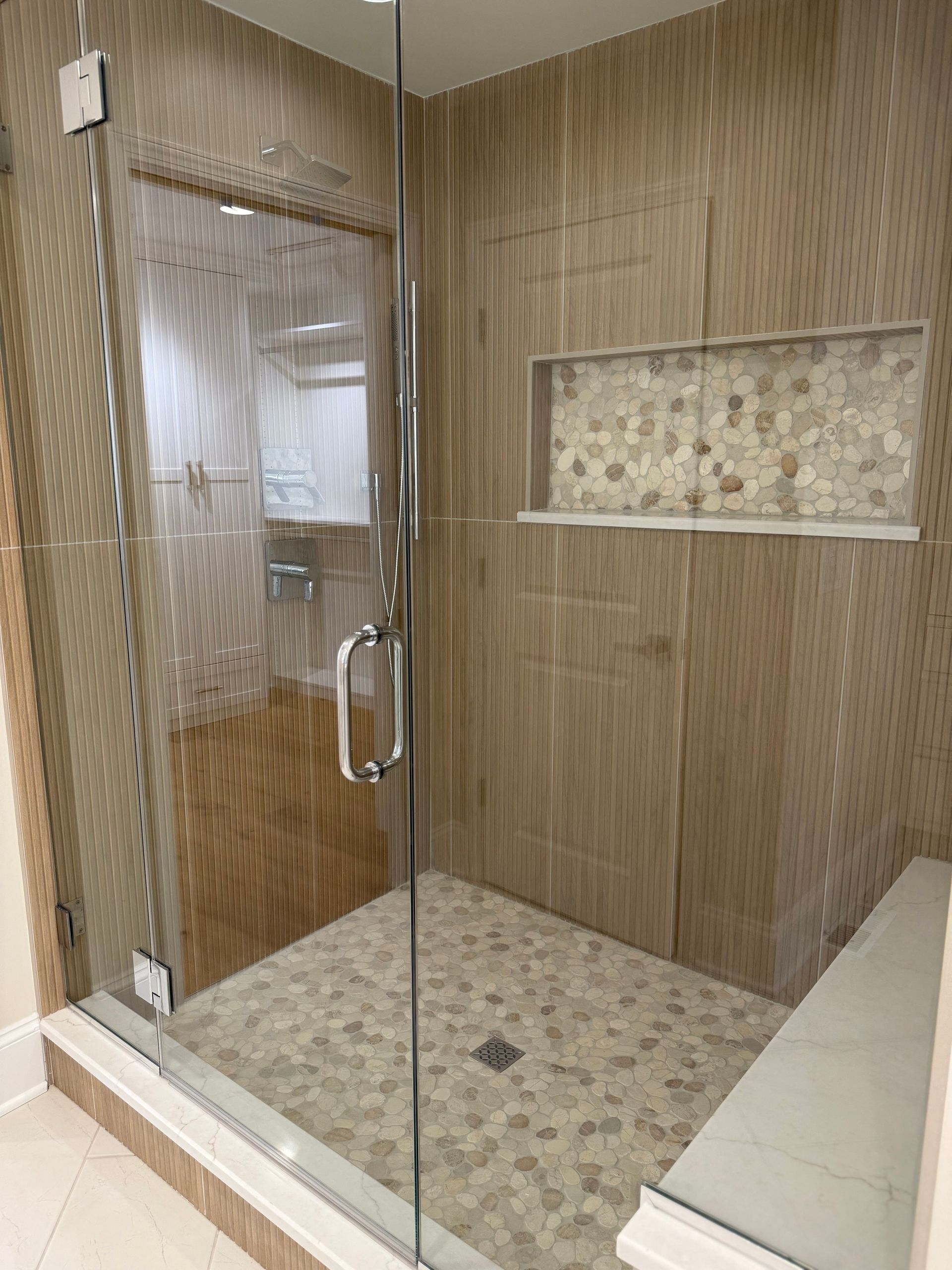 A bathroom with a walk in shower with a glass door and a bench.