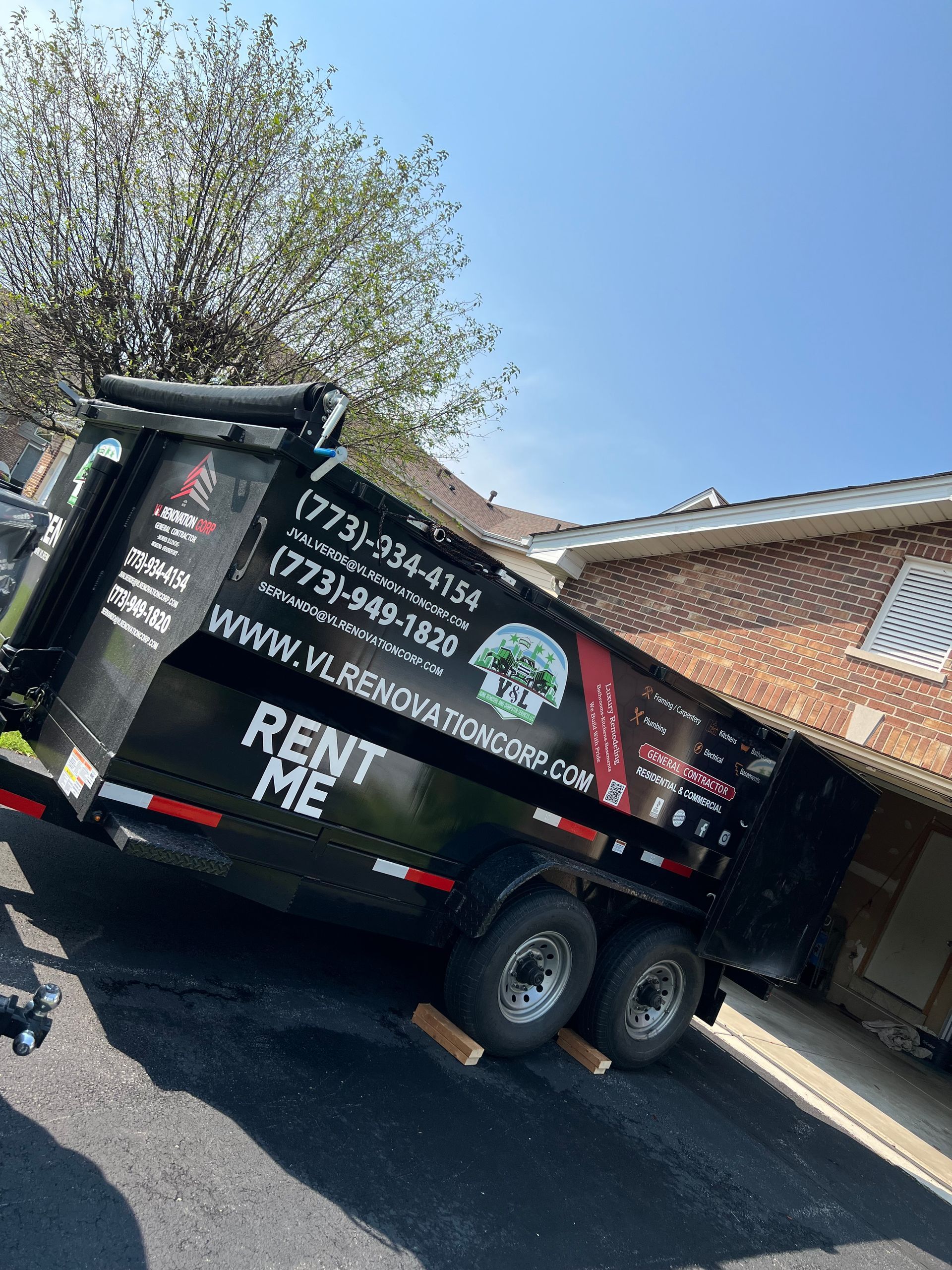 A dumpster is parked in front of a brick house.