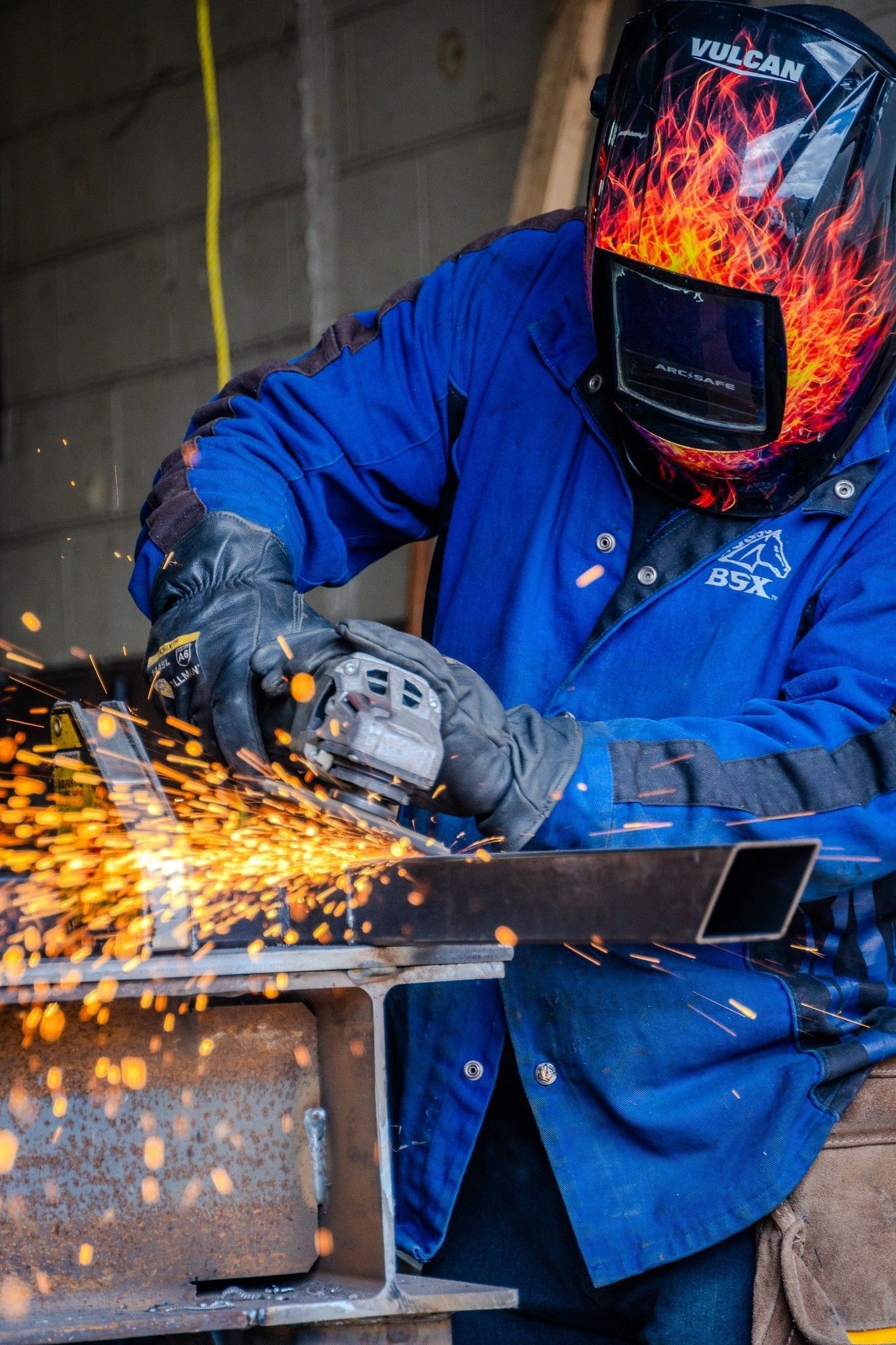 A man wearing a welding helmet is grinding a piece of metal