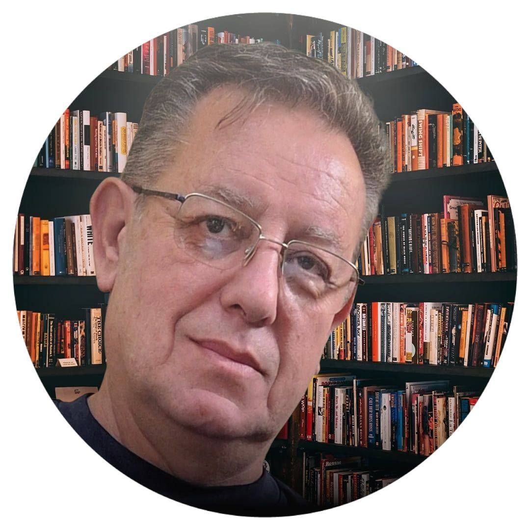 Hombre con gafas y pelo corto, con estanterías de libros de fondo.