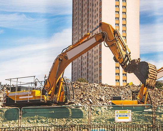 a yellow excavator is working on a construction site in front of a tall building .