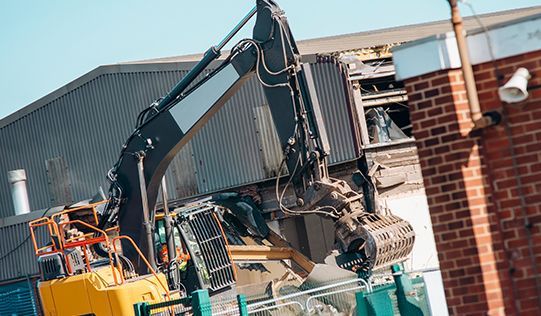 a large excavator is demolishing a brick building .