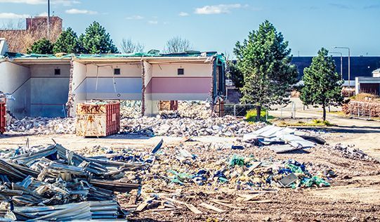 a building is being demolished and a pile of rubble is in the foreground .