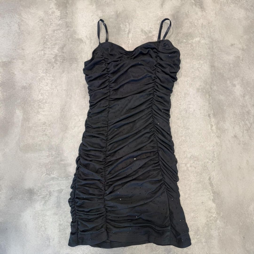 Vestido mini fruncido de color negro con tirantes finos sobre superficie gris.