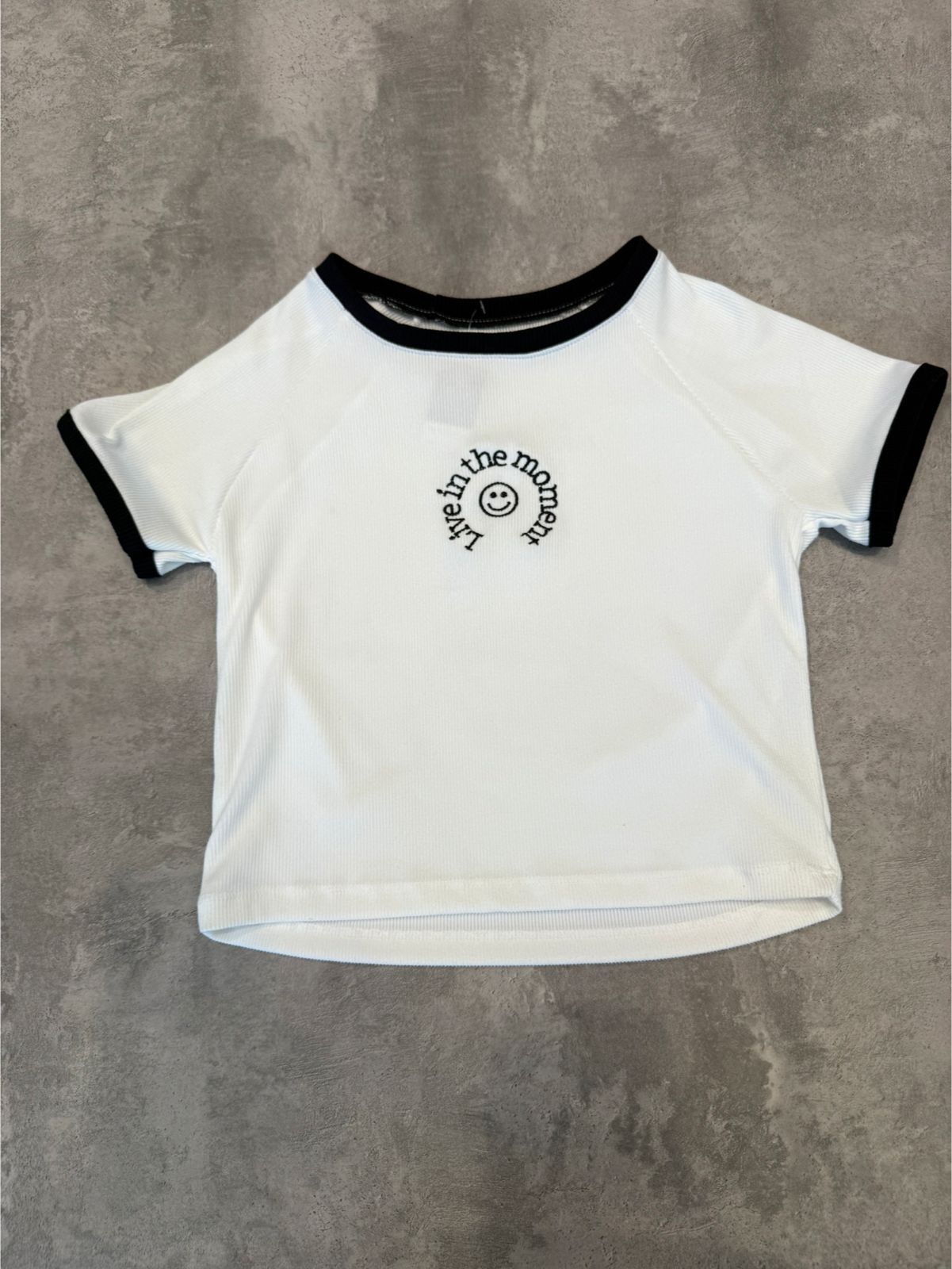 Top corto blanco con ribete negro y logotipo circular.