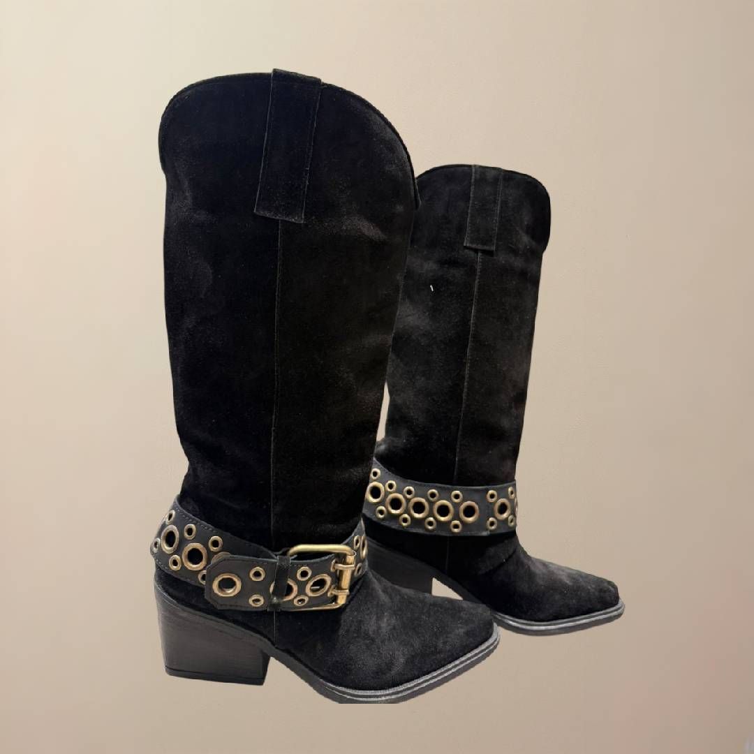 Botas estilo western de gamuza negra, hasta media pantorrilla, con detalles de herrajes dorados sobre fondo neutro.
