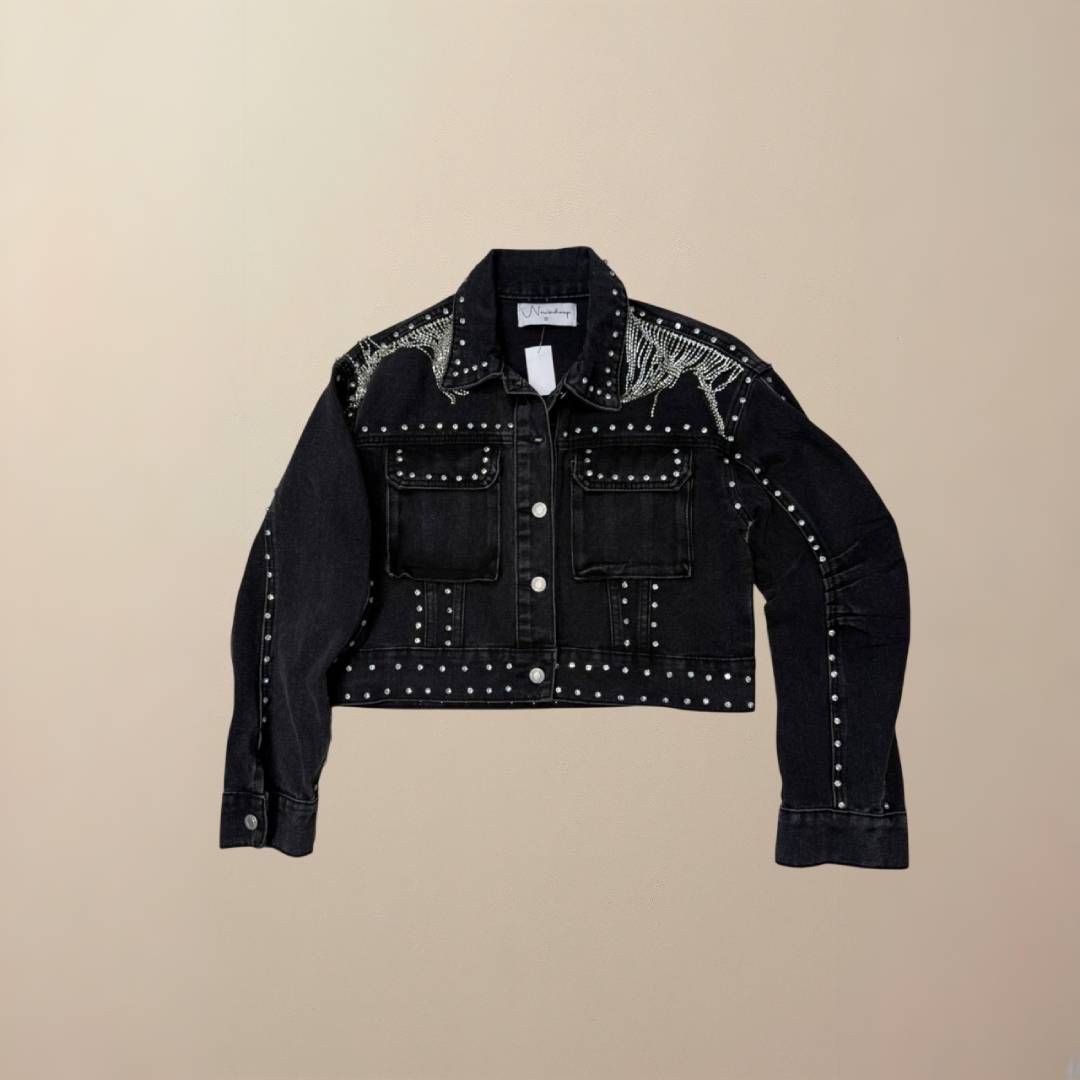 Chaqueta vaquera negra con tachuelas plateadas sobre fondo neutro.