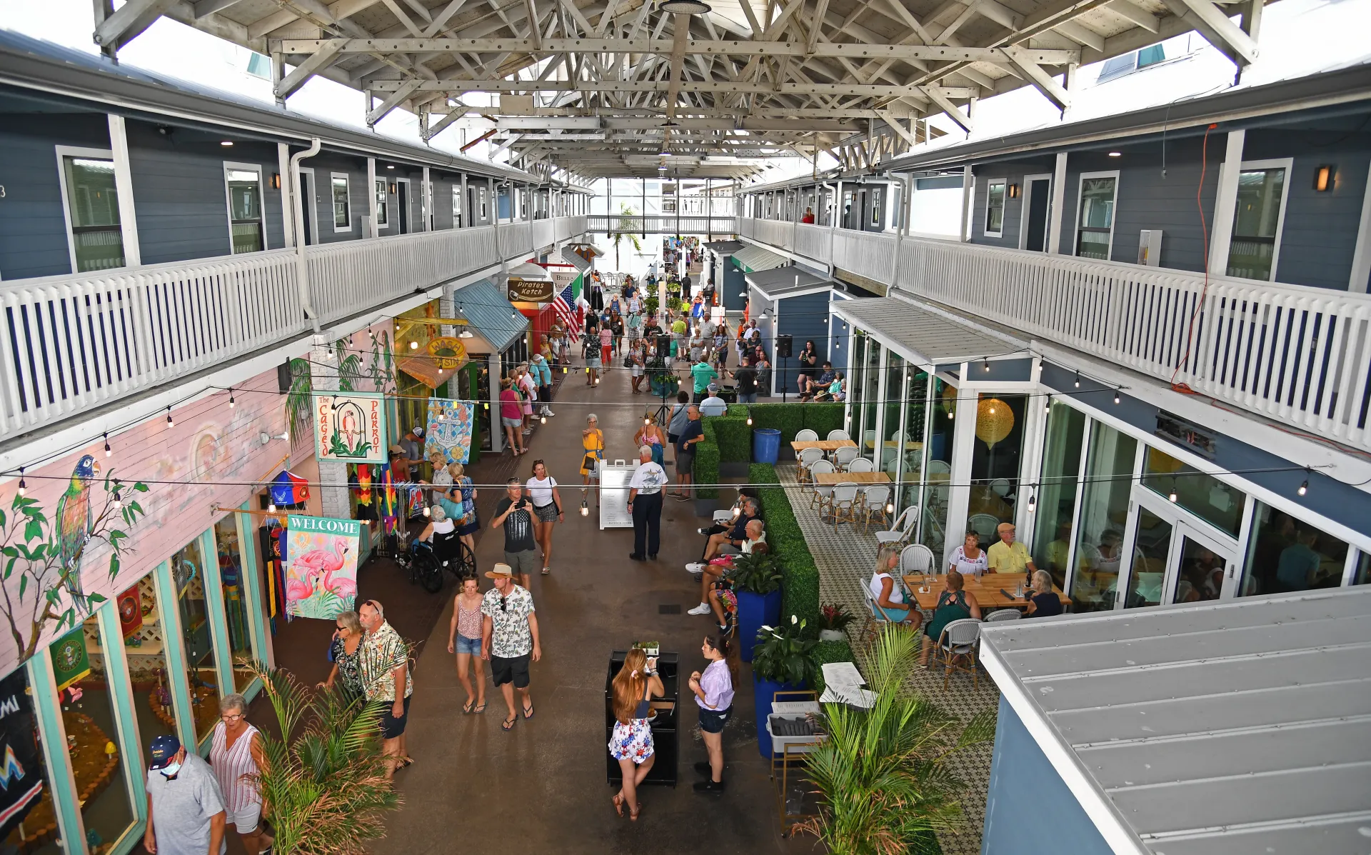 Marketplace with shops, a central walkway, and a crowd of people under a covered walkway.
