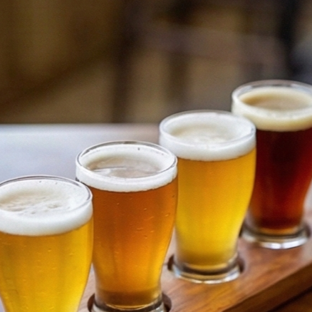 Flight of four craft beers in varying colors, served on a wooden tray.
