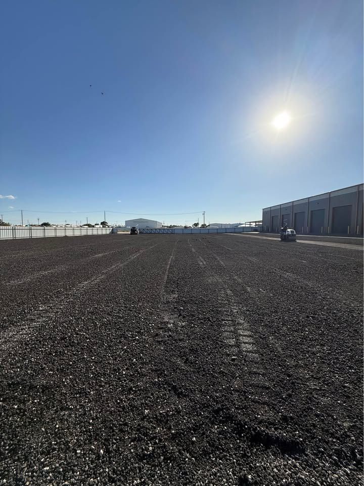 Dirt road with tire tracks, leading uphill past buildings on a sunny day.