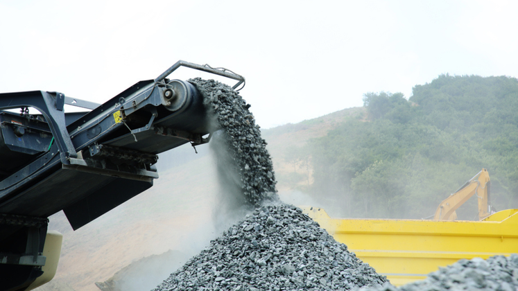 Rock crusher dispensing gravel into a yellow truck.