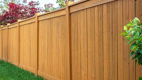 Wooden privacy fence in a backyard with green grass and foliage.