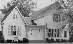 White two-story building with gabled roof, possibly a funeral home, with an American flag.