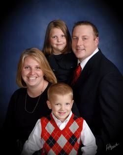 Family portrait with parents and two children, smiling against a dark blue background.