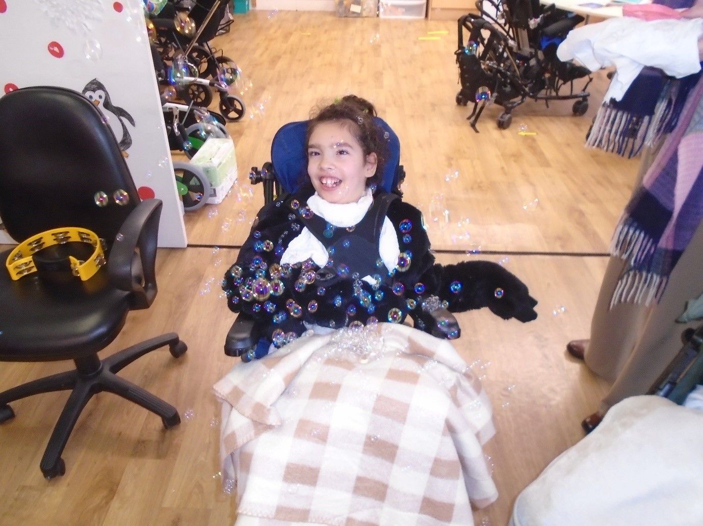 A little girl in a wheelchair is smiling in front of a mirror