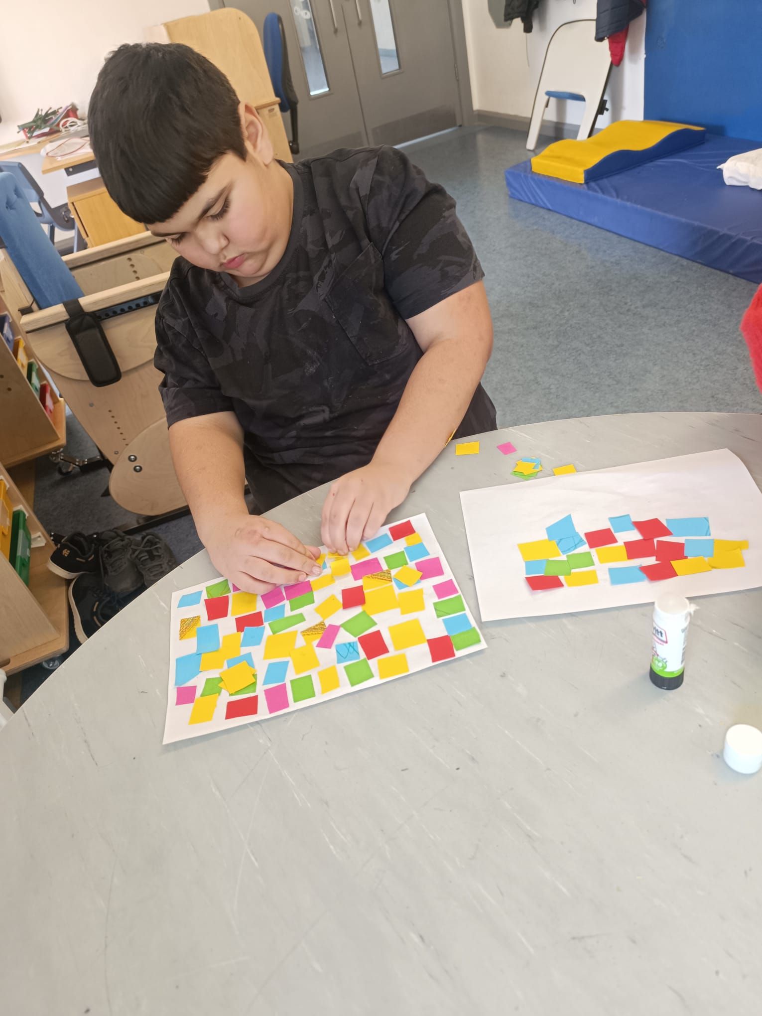 A young boy is sitting at a table playing with stickers.