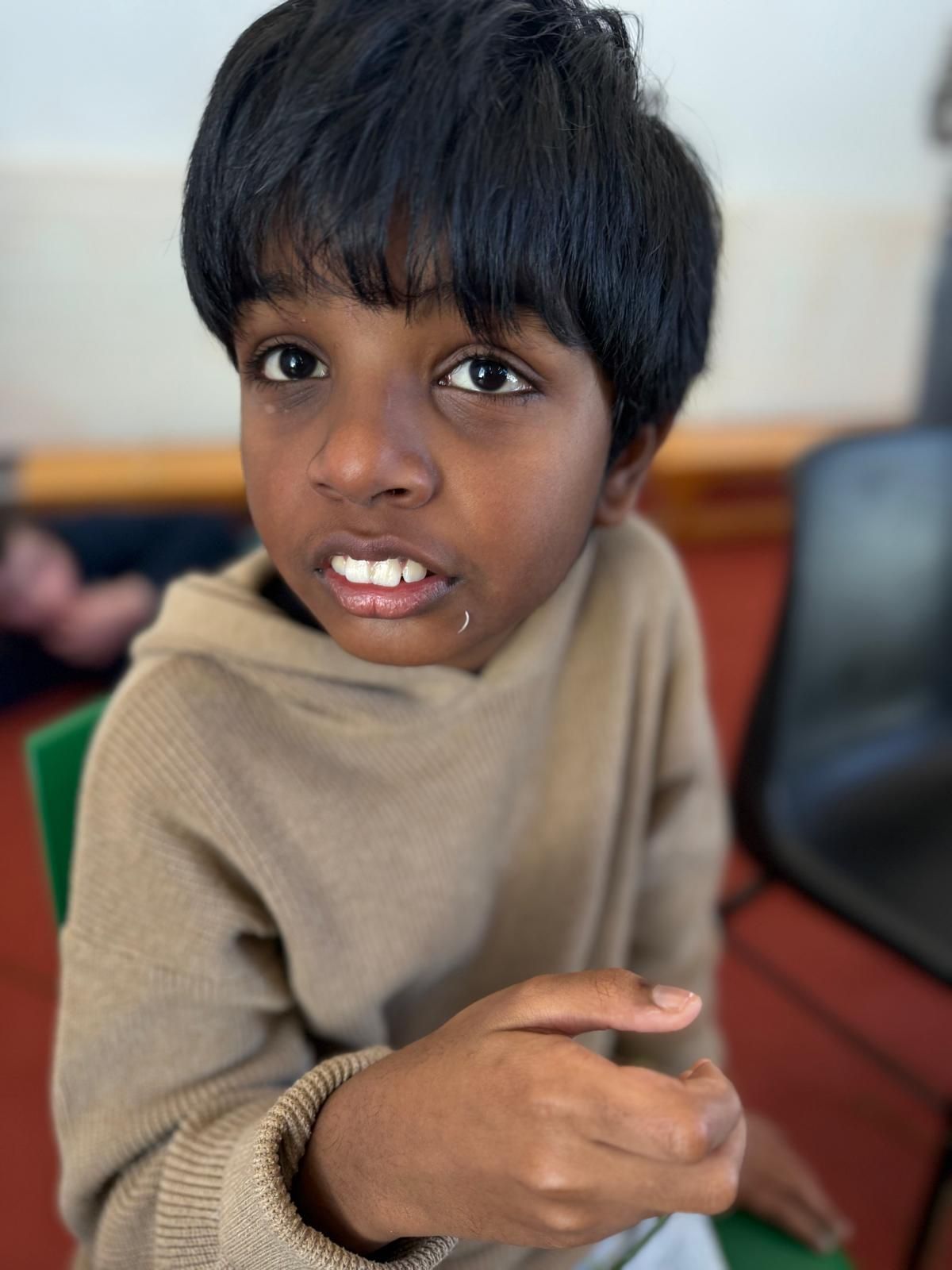 A young boy in a tan sweater is sitting in a green chair