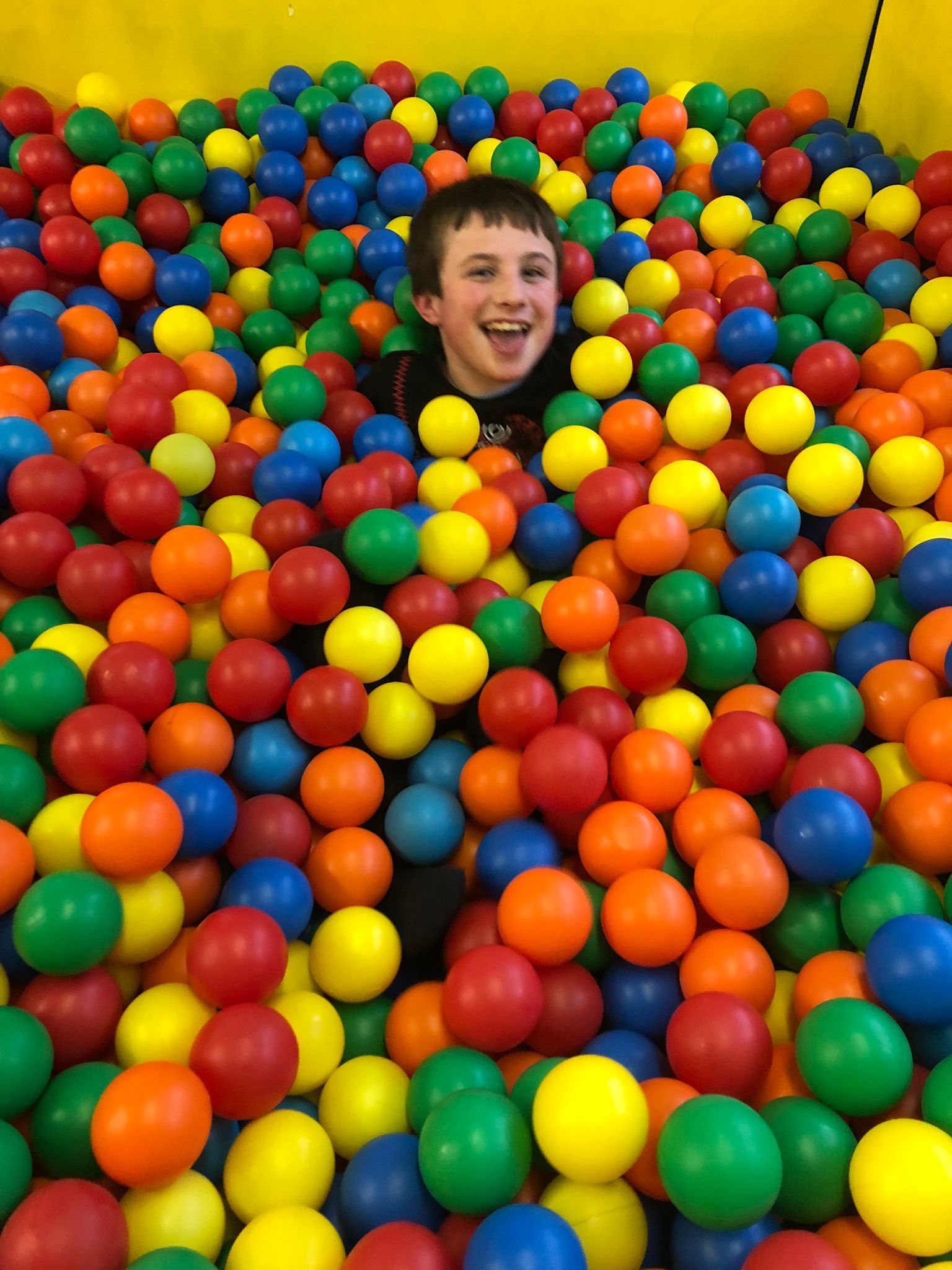 A young boy is playing in a ball pit filled with colorful plastic balls.