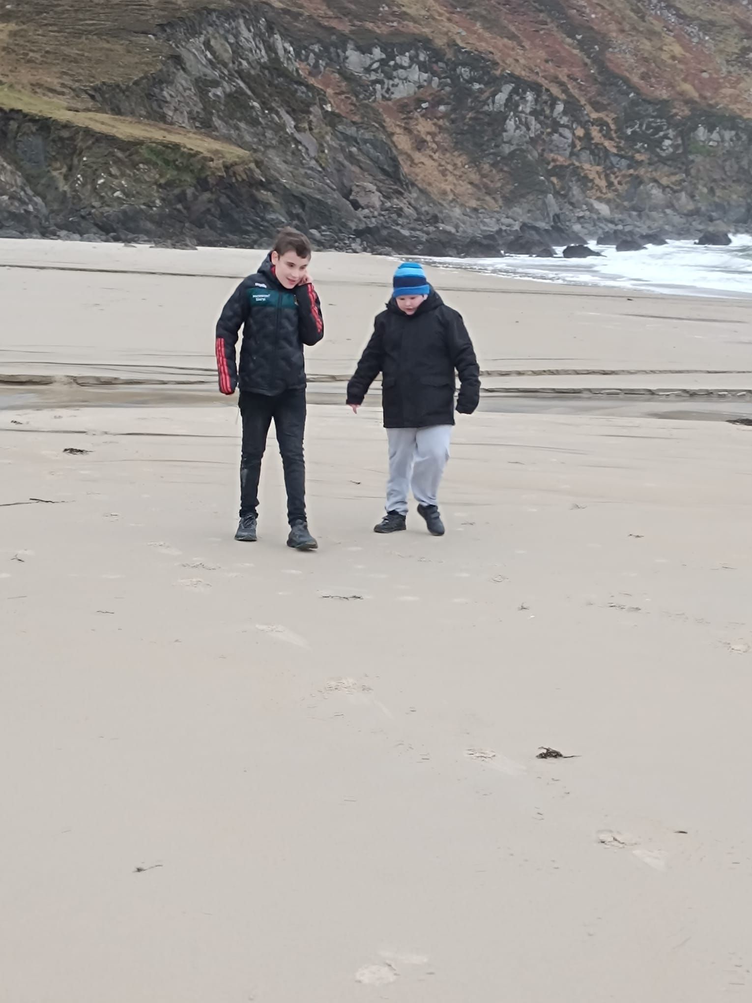 Two young boys are walking on a sandy beach.