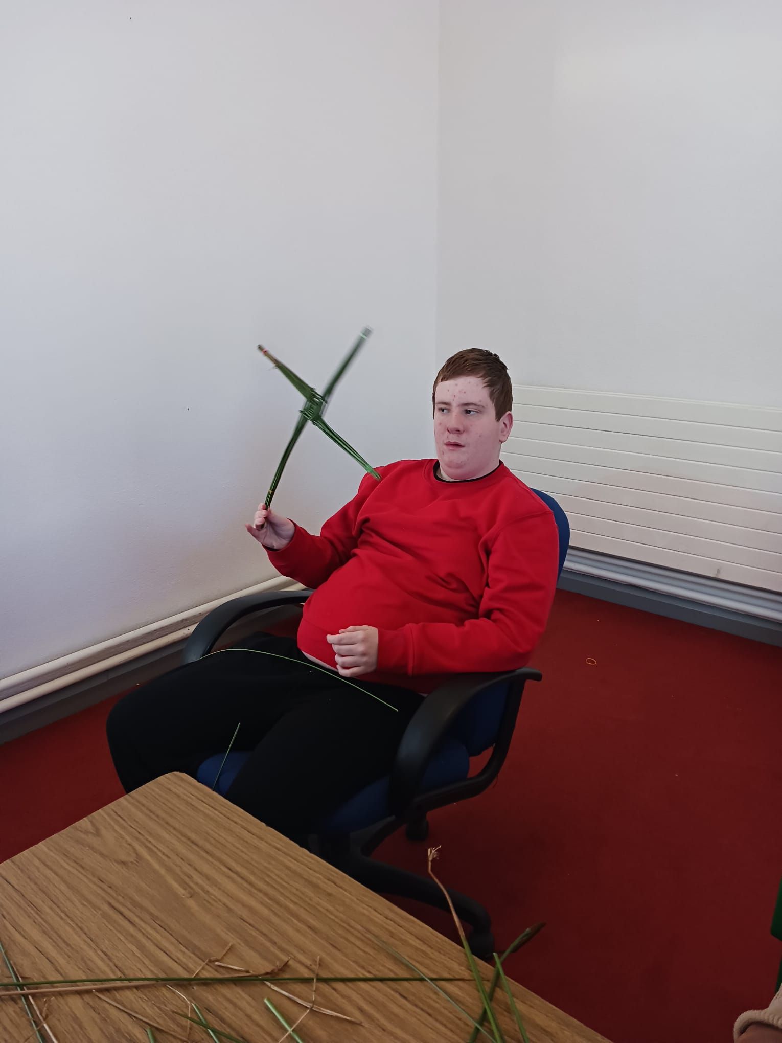 A man in a red shirt is sitting in a chair holding a green stick