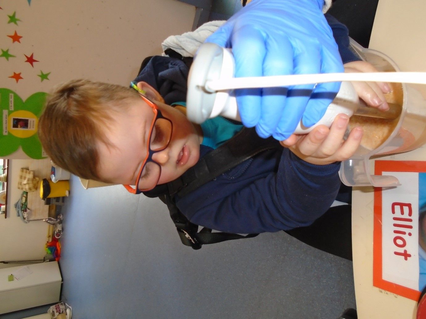 A boy wearing blue gloves is pouring something into a cup