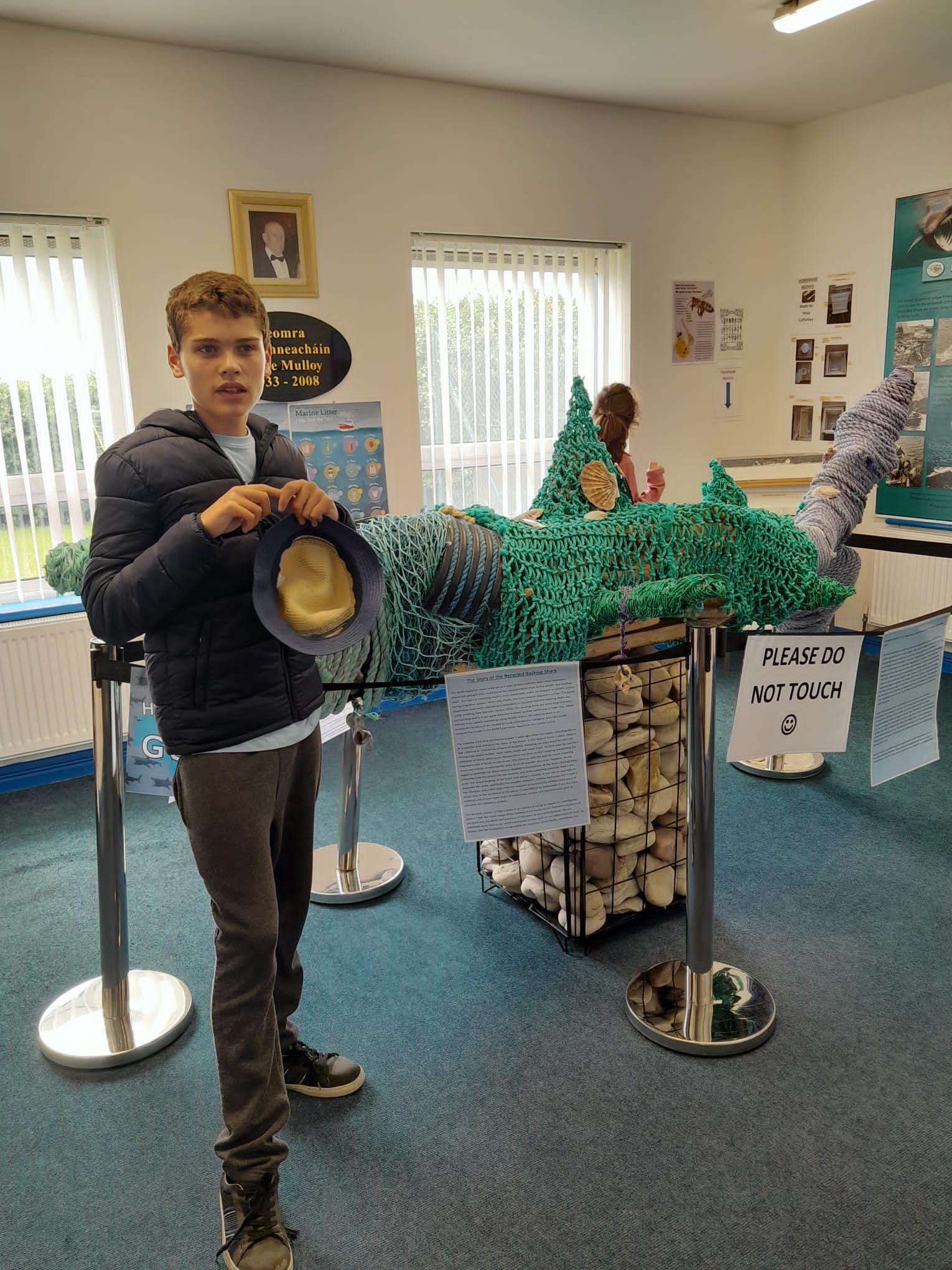 A young man is standing in a room holding a hat.