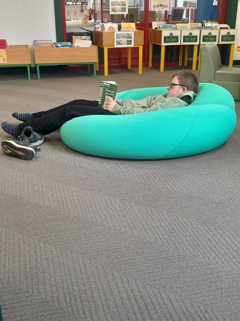 A person is laying on a green bean bag chair reading a book