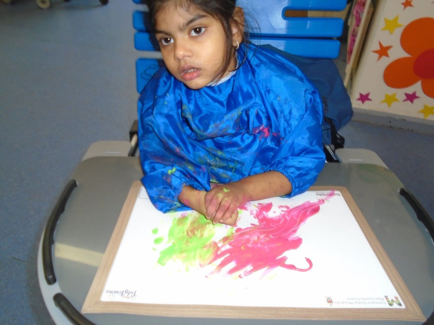 A little girl in a blue apron is painting on a piece of paper