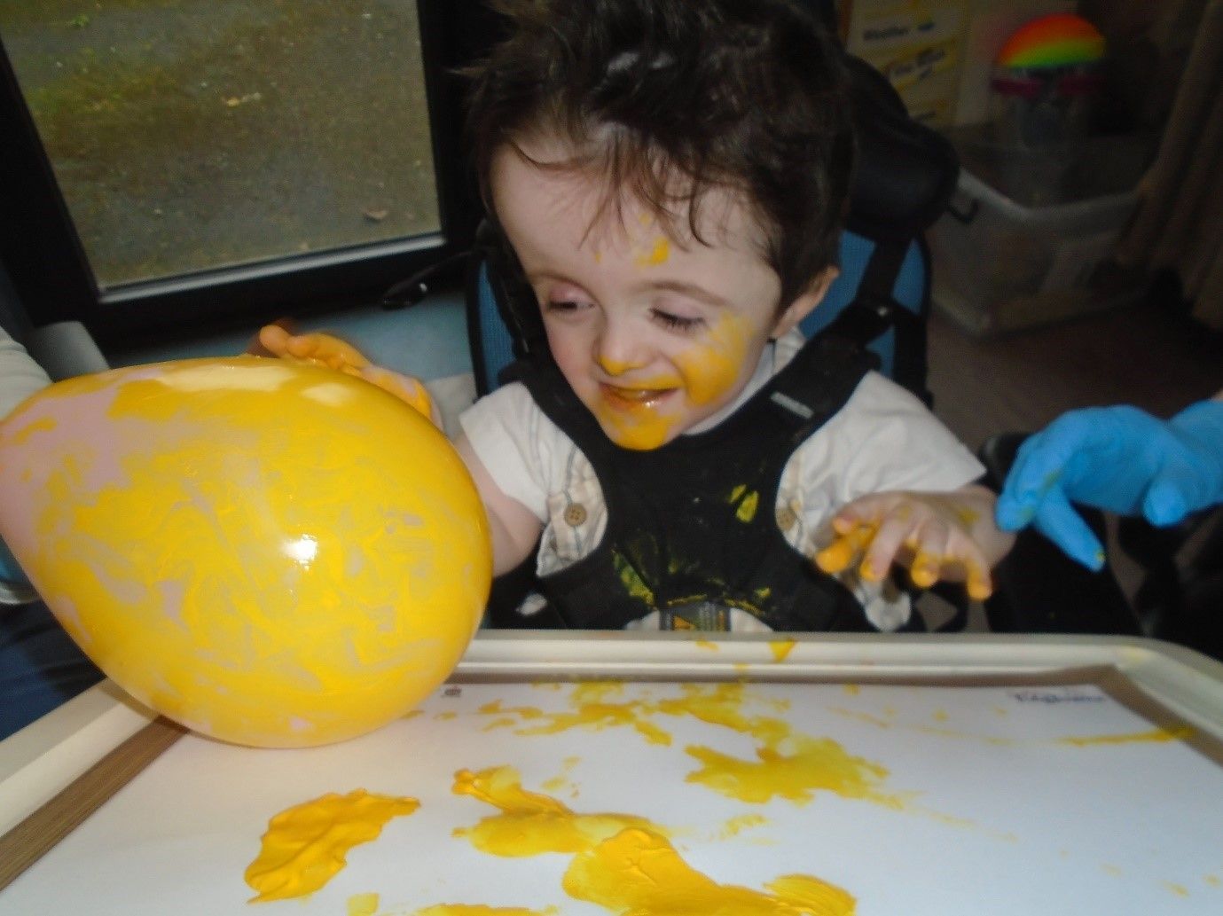 A baby in a high chair with yellow paint on his face