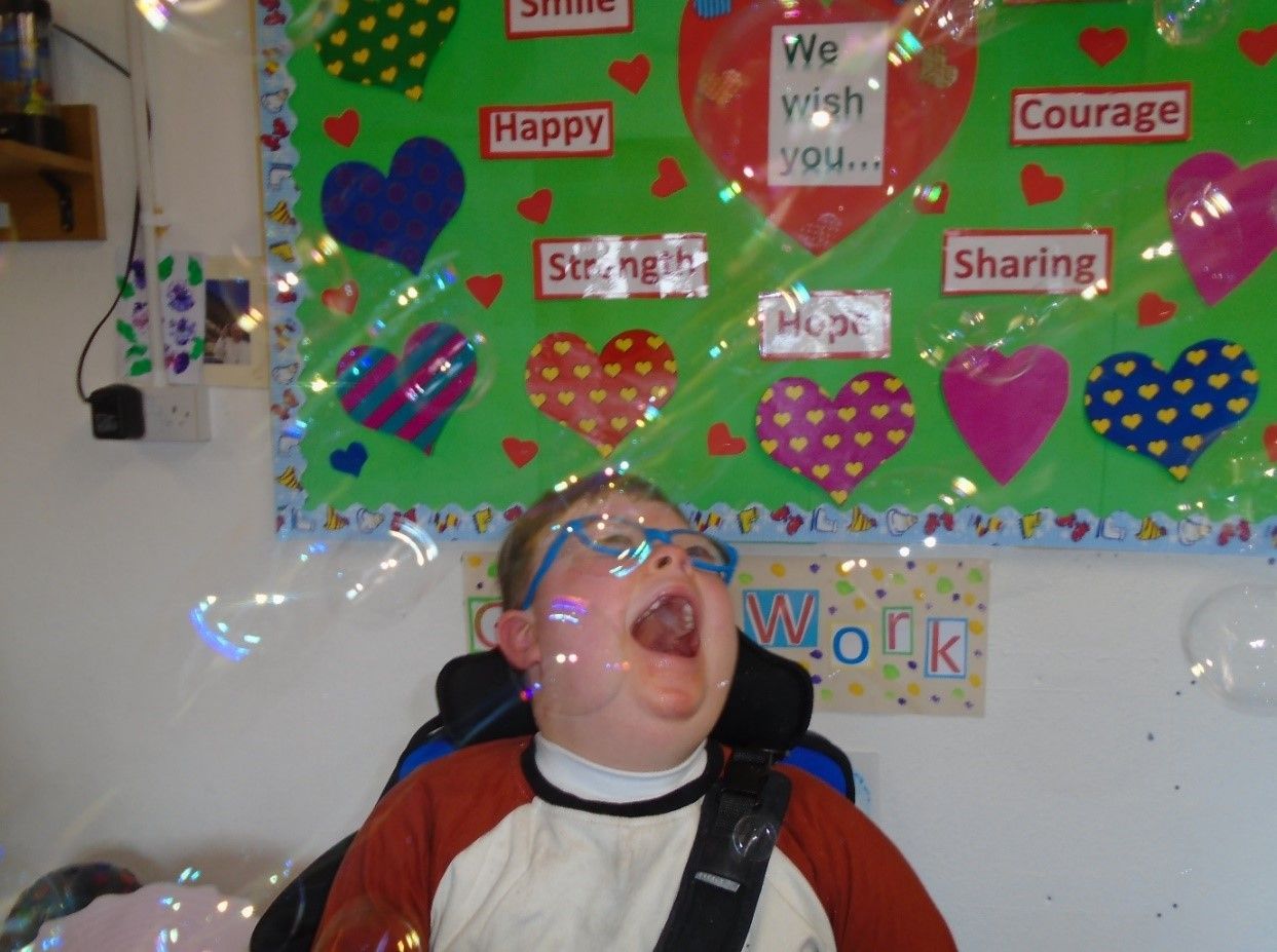 A child blowing soap bubbles in front of a bulletin board that says happy