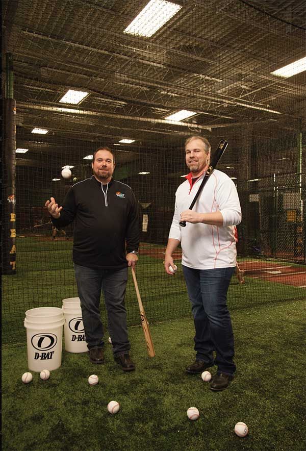 Two men are standing on a baseball field holding bats and balls.