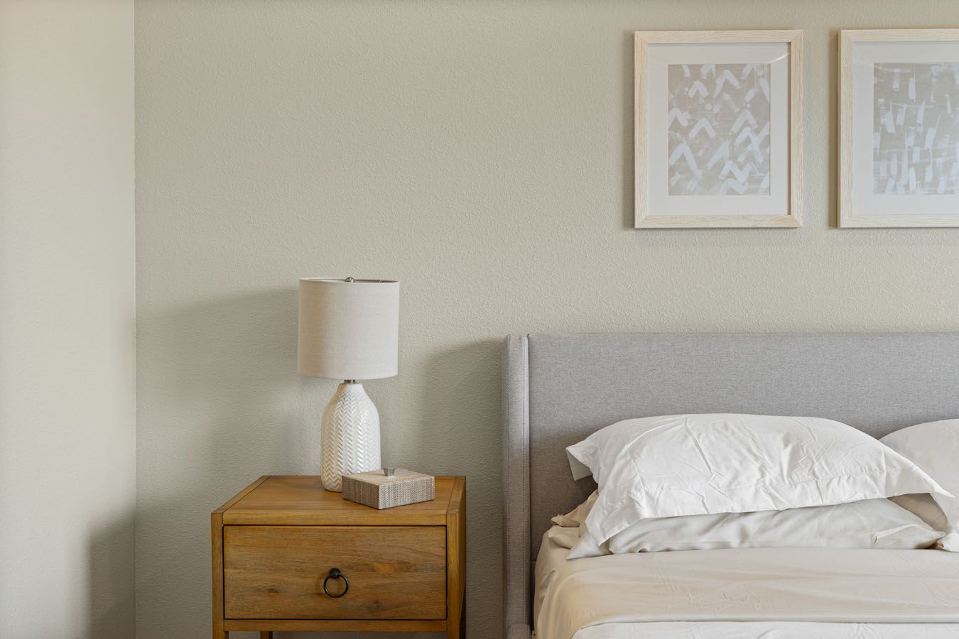 a bedroom with a bed , nightstand , lamp and two paintings on the wall .