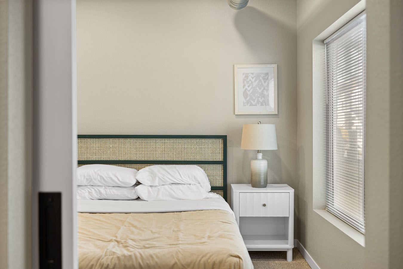 a bedroom with a bed , nightstand , lamp and window .