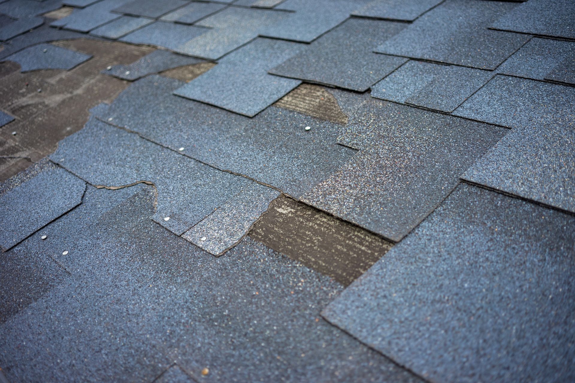 Roofing worker installing dark shingles on a house roof beside a brick chimney