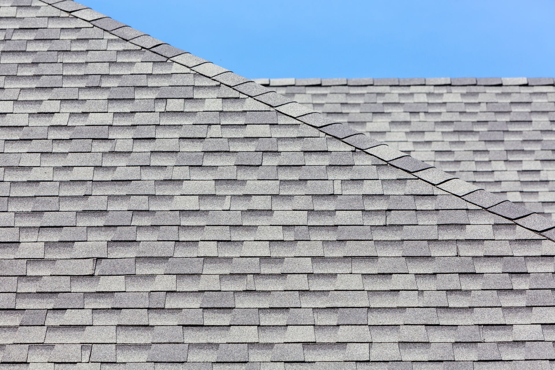 Roofing workers installing shingles on a sloped roof, one hammering in the foreground and one kneeling behind.