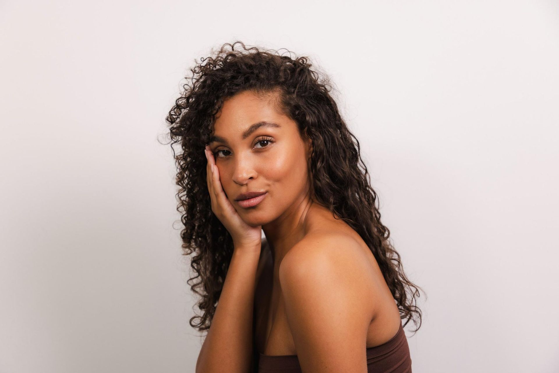 Woman With Curly Hair is Holding Her Hand to Her Face — CIMED Aesthetics in Newcastle, NSW