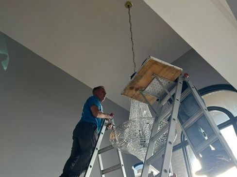 A man standing on a ladder working on a chandelier
